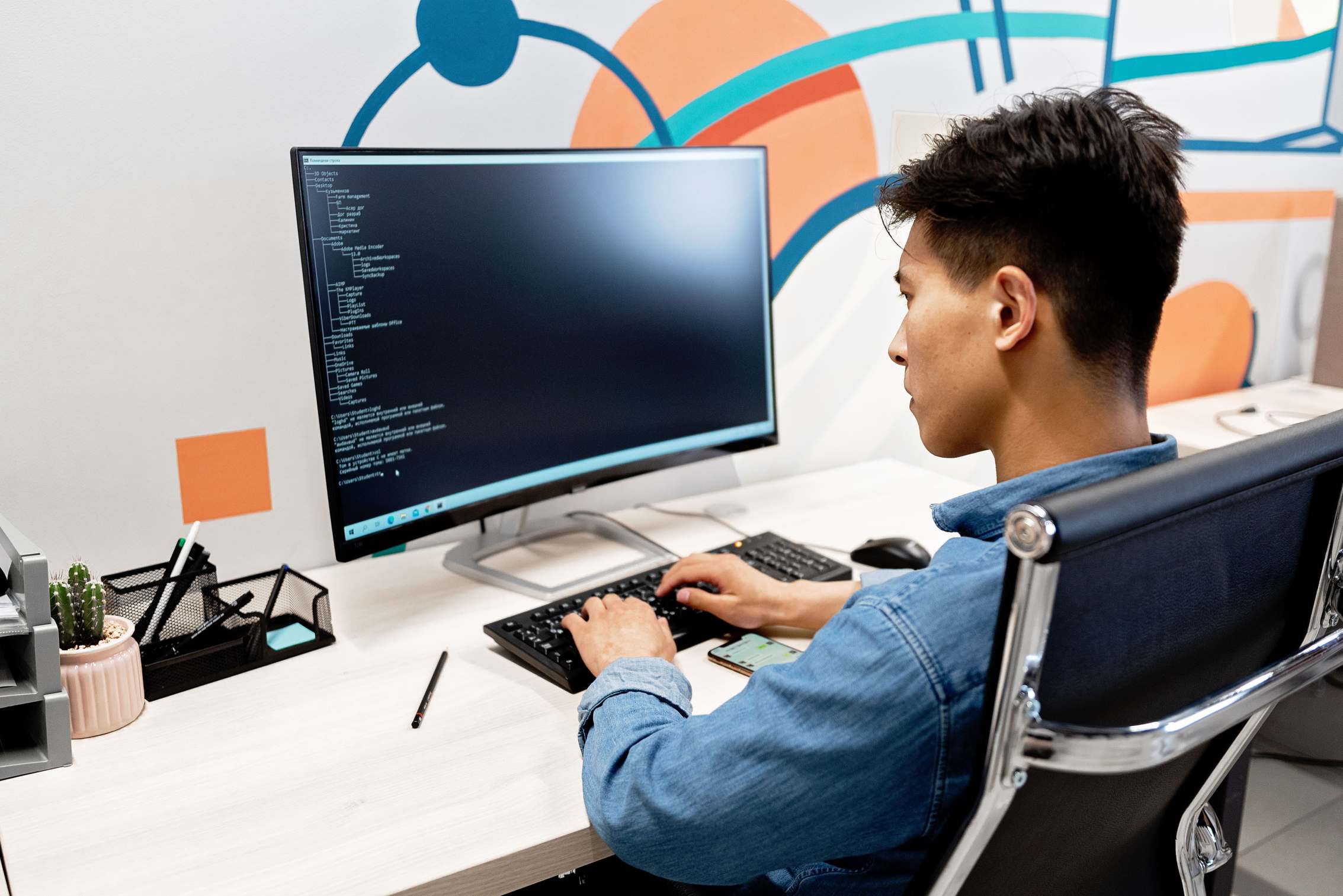 Wide view of a software engineering workspace with monitors and a programmer at a desk